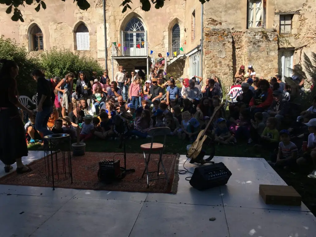 En plein air, une scène avec un siège et une guitare, le public autour